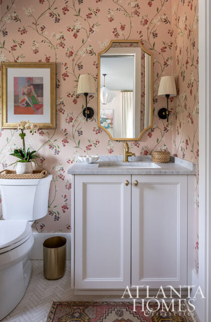 Powder room with pink floral wallpaper, white vanity, marble countertop, gold mirror, and brass