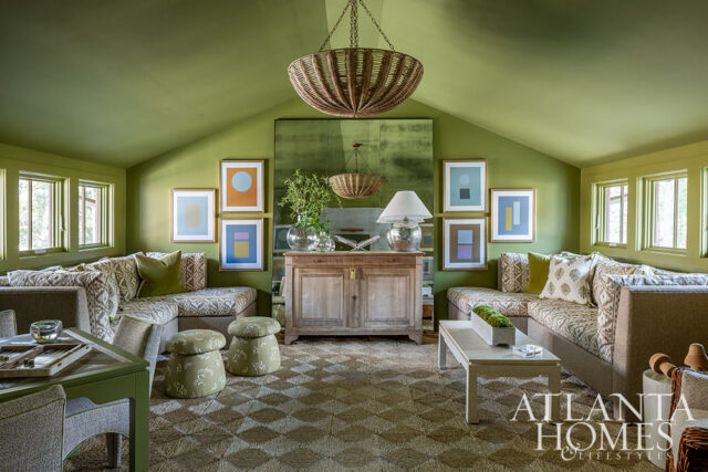 Green living room with sectional sofa, abstract art, woven pendant light, and mirrored cabinet.