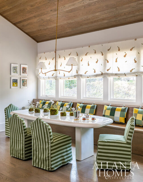 Dining room with oval table, green striped chairs, banquette seating, and pear-patterned window