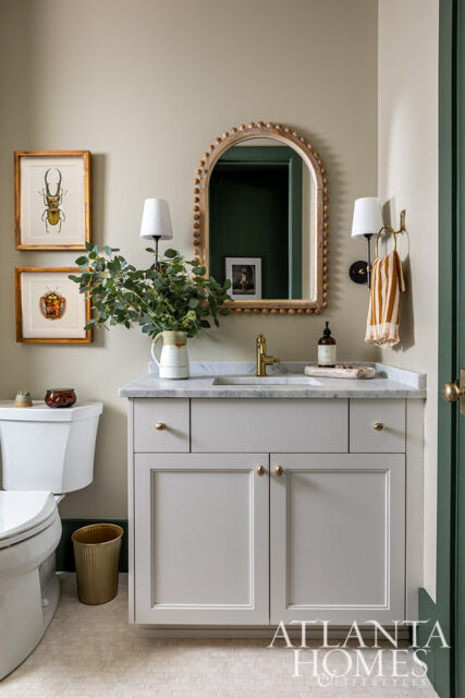 Powder room with light gray vanity, marble countertop, brass faucet, and framed insect art.