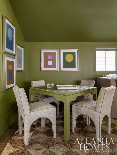 Green game table with four upholstered chairs and abstract art on olive green walls.