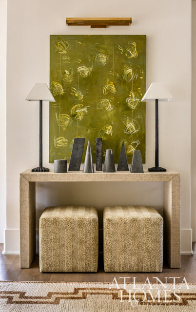 Console table with abstract green painting, two lamps, and geometric sculptures.