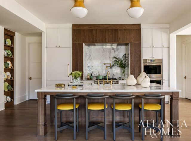 Kitchen island with marble countertop, yellow bar stools, and wood cabinetry. Marble backsplash and