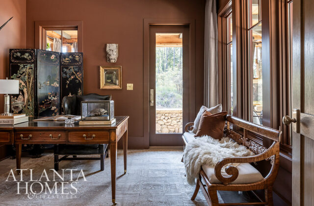 Brown room with antique desk, folding screen, glass display case, and wooden bench with pillows and