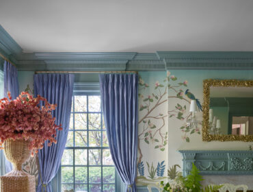 Dining room with blue curtains, floral wallpaper, and a wooden table set with dishes.