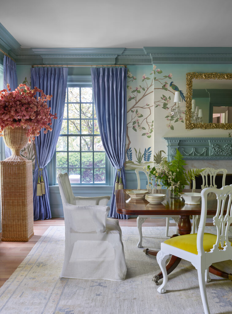 Dining room with blue curtains, floral wallpaper, and a wooden table set with dishes.