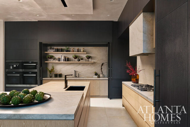 Modern kitchen with dark cabinetry, marble countertops, and light wood accents. Features built-in