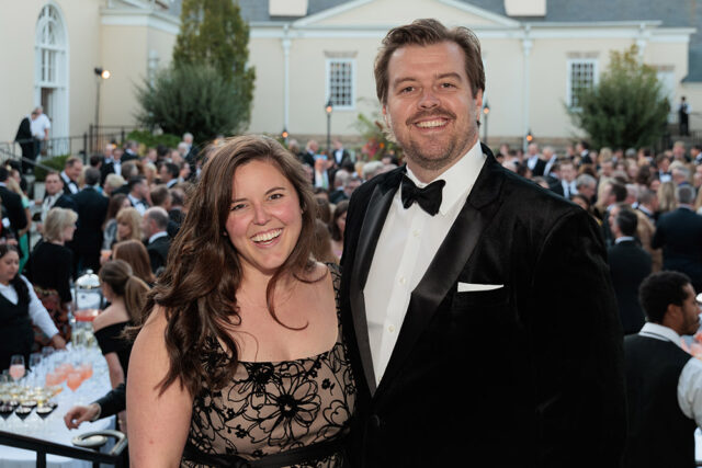 Man in tuxedo and woman in patterned dress smiling at event