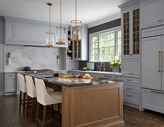 Gray kitchen with marble backsplash, wood island, and brass pendant lights.