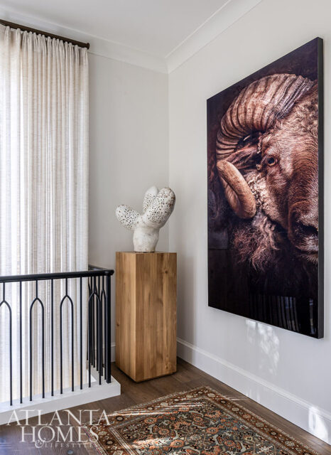 Hallway with large ram portrait, sculpture on wooden pedestal, and oriental rug