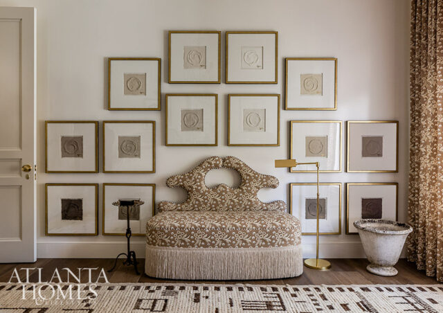Living room with a patterned bench, gallery wall of framed art, and fringed rug.