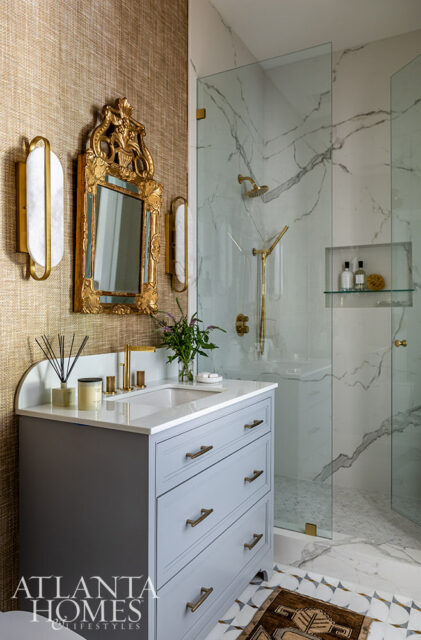 Gray vanity with brass hardware, marble shower, and gold ornate mirror.