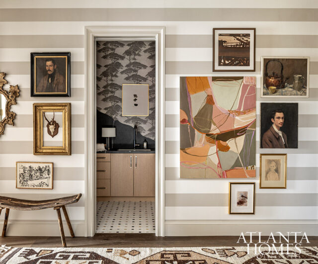 Hallway with striped wallpaper, eclectic art, and a wet bar visible through doorway.