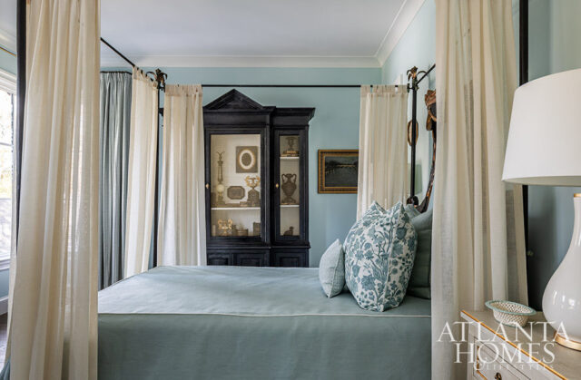Bedroom with a four-poster bed, light blue walls, and a black curio cabinet filled with decorative