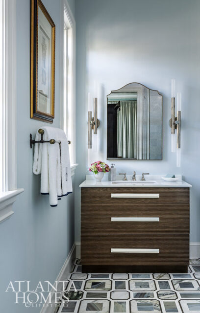Powder room with light blue walls, wood vanity, marble countertop, and geometric floor tiles.