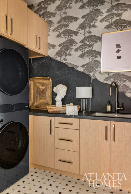 Laundry room with stacked black washer and dryer, light wood cabinets, dark stone backsplash, and