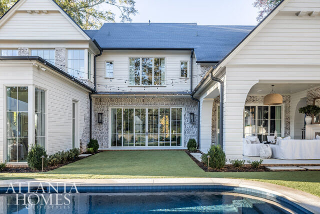 White house with brick accents, large windows, string lights, and a covered patio overlooking a