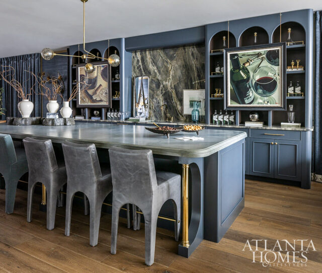 Dark blue kitchen island with gray bar stools, marble countertop, and arched shelving with artwork