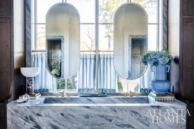 Marble bathroom vanity with double oval mirrors, brass faucets, and blue hydrangeas
