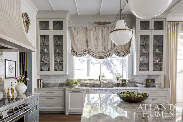 Gray and white kitchen with marble countertops, glass-front cabinets, and a large island.