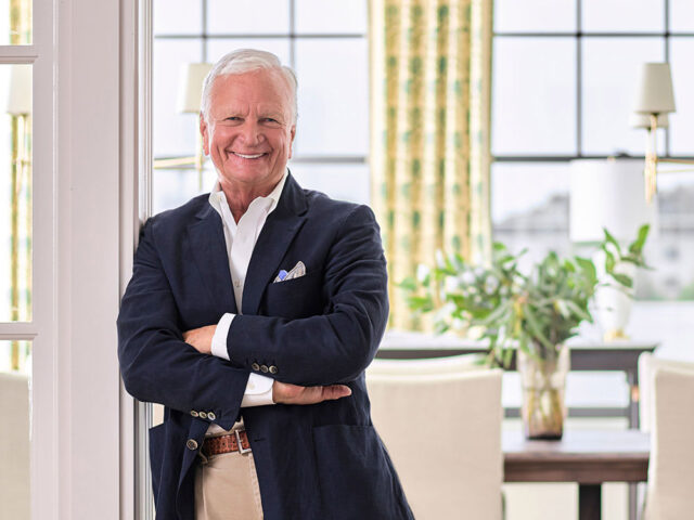 Man in navy blazer and khaki pants smiling with arms crossed.