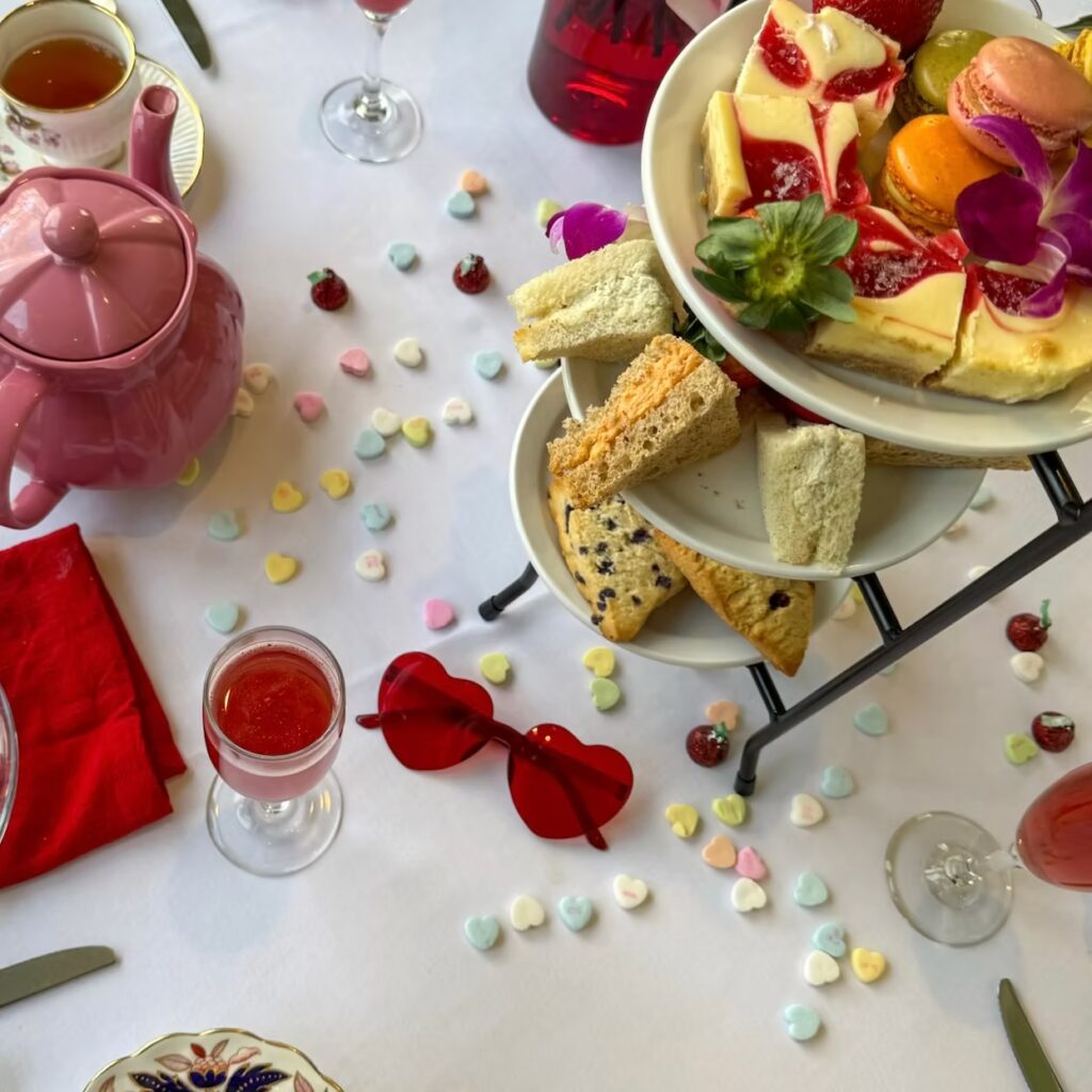 Heart-shaped red sunglasses on a white tablecloth with candy hearts and a tiered dessert stand