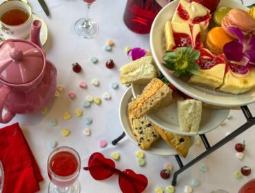 Heart-shaped red sunglasses on a white tablecloth with candy hearts and a tiered dessert stand