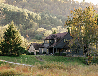 Dark gray house with stone accents nestled in a grassy hillside with trees.