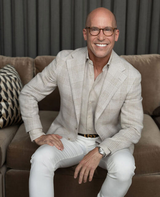 Man in a plaid blazer and white pants sitting on a sofa.