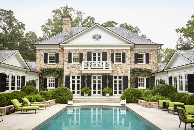 Stone house with black shutters, white trim, and a balcony overlooking a pool