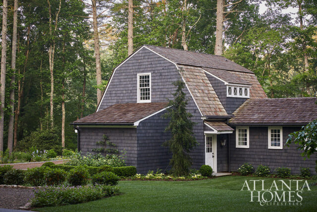 Dark gray shingle-sided house with wood shake roof and white windows.