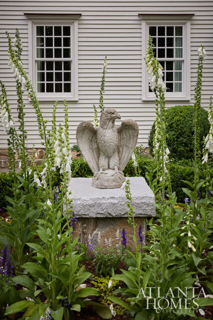 Stone eagle statue in garden with foxglove and two windows on clapboard house
