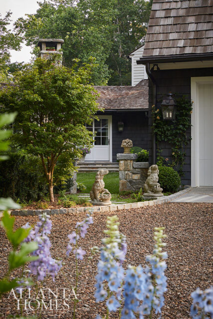 Dark shingle exterior with stone chimney, dog statues, and gravel driveway.