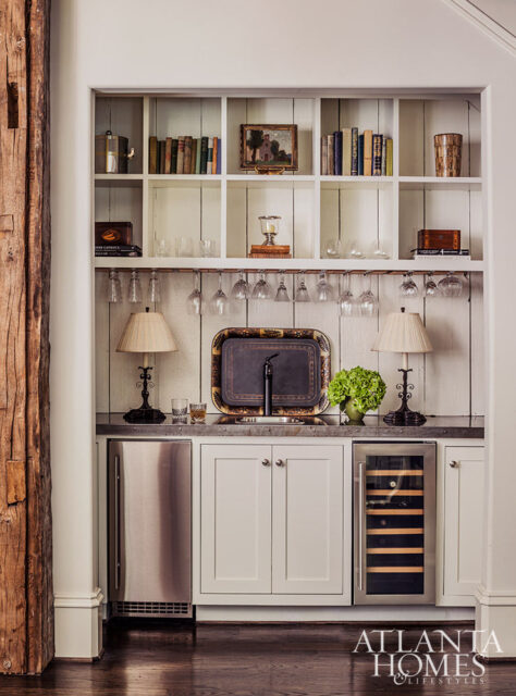 Built-in bar with white cabinetry, stainless steel mini-fridge, wine fridge, and shelves stocked