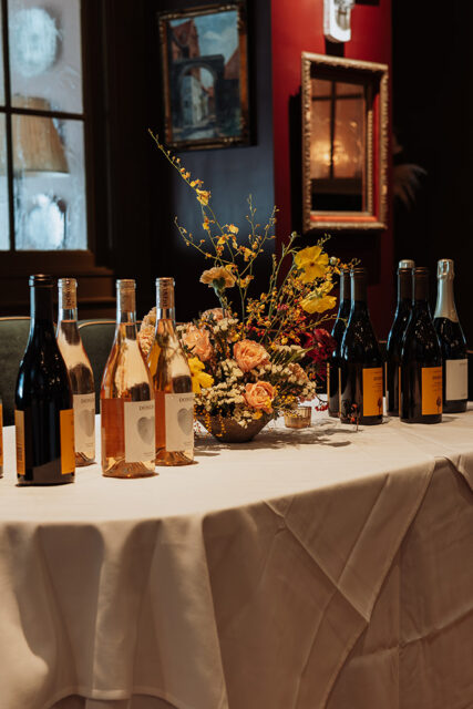 Table with wine bottles and floral arrangement, framed art on wall