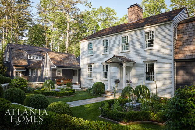 White clapboard house with cedar shake roof and manicured gardens.