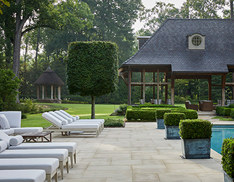 Patio with lounge chairs and pool, adjacent to a covered outdoor living space and manicured lawn.