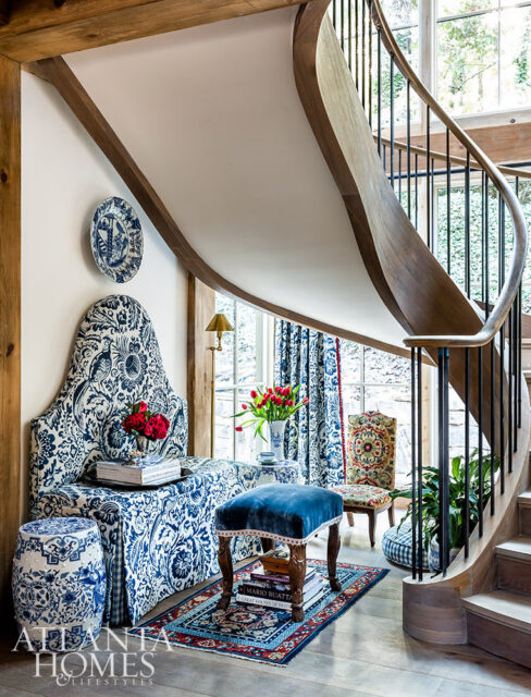 Entryway with a curved wooden staircase, blue and white patterned upholstered bench, blue velvet ottoman, and a ceramic garden stool.