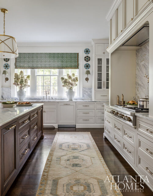 Luxury kitchen with dark wood island, white cabinetry, marble countertops, a patterned runner rug, and a large range with a decorative hood.