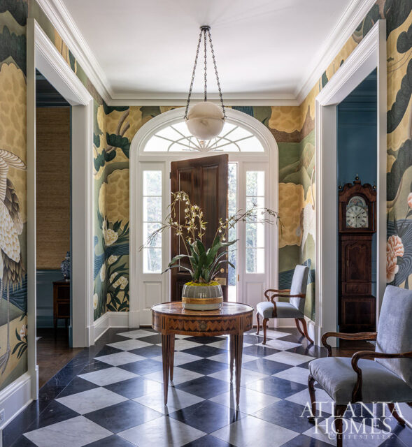 Foyer with black and white checkered marble floor, arched doorway with a dark wood door, patterned wallpaper, and two upholstered chairs.