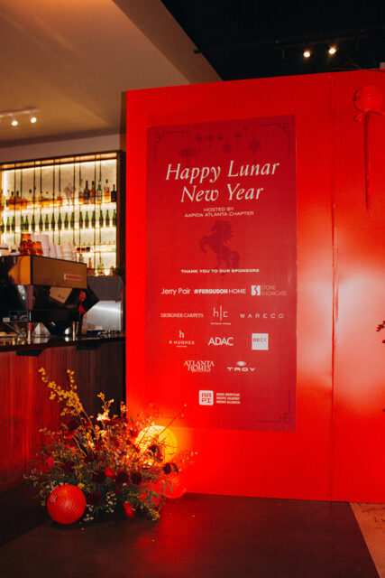 Red backdrop with 'Happy Lunar New Year' text, hosted by AAPIDA Atlanta Chapter, and listing sponsors including Ferguson Home, Stone Showcase, Designer Carpets, Wareco, R Hughes, ADAC, Beck, Atlanta Homes, Troy, and Asian American Pacific Islander Design Alliance.
