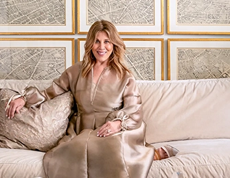 Woman in a champagne-colored satin dress sitting on a cream sofa in front of a wall of framed maps.
