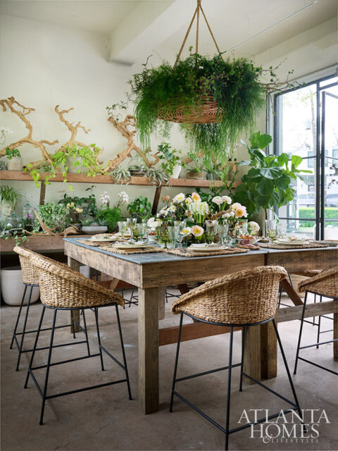 Dining room with rustic table, woven chairs, and abundant plants.