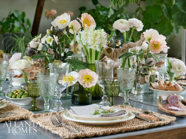 Table setting with floral arrangements, green and clear glassware, olives, and charcuterie.