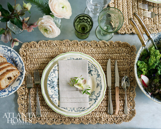 Table setting with blue and white plates, woven placemat, linen napkin, and floral arrangement.