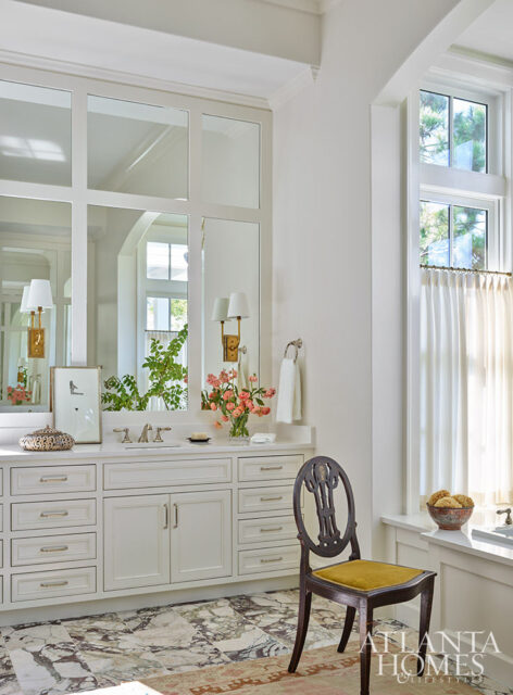 White bathroom vanity with marble floor, ornate chair, and large mirrors.