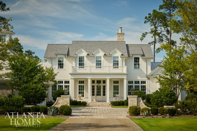 White clapboard house with gray roof, stone accents, and manicured landscaping.