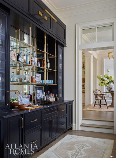 Black bar cabinet with brass hardware and glass shelves displaying liquor bottles.