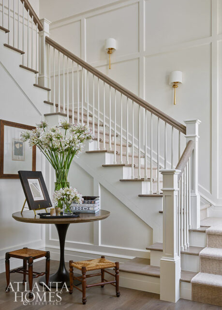 White staircase with wood banister, carpeted steps, and two gold sconces.