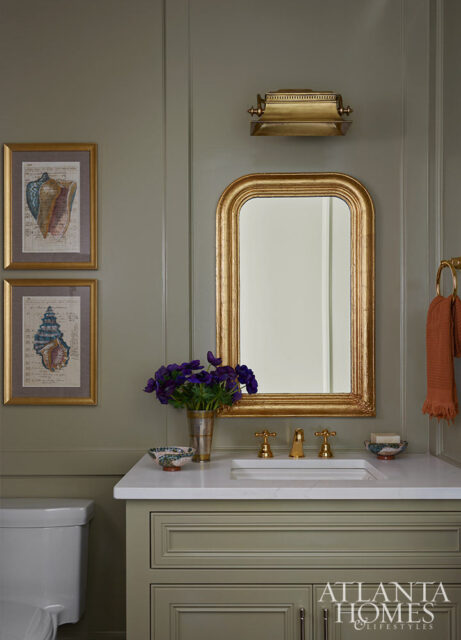 Bathroom with sage green vanity, gold mirror, and framed seashell prints